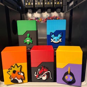 Könnte beinhalten: Fünf rechteckige Aufbewahrungsboxen in verschiedenen Farben, jede mit einem einzigartigen erhabenen Charakter-Emblem auf der Vorderseite. Die Boxen sind grün-grau, blau-dunkelblau, orange-gelb, rot-grau sowie gelb-lila gefärbt.