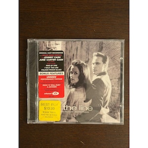 Op de afbeelding: Een cd-hoesje voor de soundtrack van Walk the Line met een zwart-witafbeelding van een man en een vrouw. De hoes bevat een zwart tekstvak met Johnny Cash en June Carter Cash, een rode sticker en een gele sticker op de voorzijde.