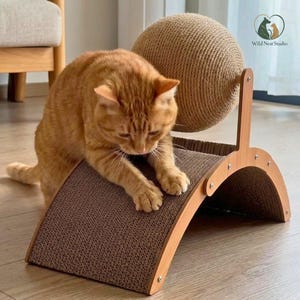 May include: A cat scratching toy featuring a curved, brown corrugated cardboard base and a large, round, tan sisal rope ball mounted on a light-colored wooden frame. The structure is designed for feline claw maintenance and play.