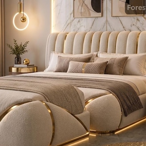 May include: A cream-coloured upholstered bed frame with a vertical channel-tufted headboard and gold metal accents. The bed features integrated under-bed lighting, a textured beige throw blanket, and several decorative pillows in shades of brown.