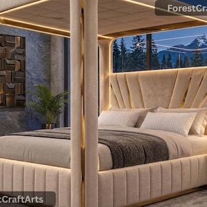 Puede incluir: Una cama con dosel tapizada en color beige con detalles en metal dorado e iluminación LED integrada. El cabecero presenta un diseño de paneles en forma de abanico, y la cama está vestida con almohadas blancas y una manta gris oscuro. Texto ForestCraftArts visible.