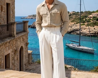 May include: A beige long-sleeved button-down shirt with two chest pockets and white wide-leg trousers. The outfit is paired with light-colored shoes and dark-tinted sunglasses, creating a coordinated look with a collared neckline and pleated waist.