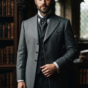 May include: A charcoal grey wool overcoat worn over a black waistcoat and trousers. The ensemble includes a white collared shirt, a black cravat with a small silver pin, and long sleeves with white cuffs visible at the wrists of the overcoat.