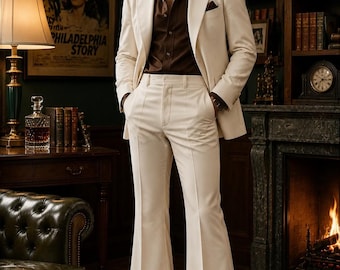 May include: A cream-colored suit featuring a blazer with wide lapels and matching high-waisted flared trousers, paired with a dark brown button-down shirt. The ensemble includes a dark brown pocket square tucked into the blazer's chest pocket.