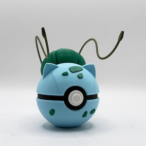 May include: A light blue spherical object with a black horizontal band and a central white button. It features dark green spots on the surface, a dark green bulb-like structure on top, and two thin, curved dark green antennae extending upwards.