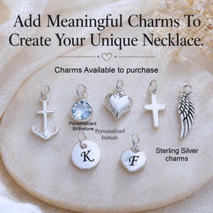 May include: A collection of seven silver-toned charms including an anchor, a light blue crystal, a heart, a cross, a wing, and two circular and heart-shaped discs engraved with the letters K and F. Text reads: Add Meaningful Charms To Create Your Unique Necklace.