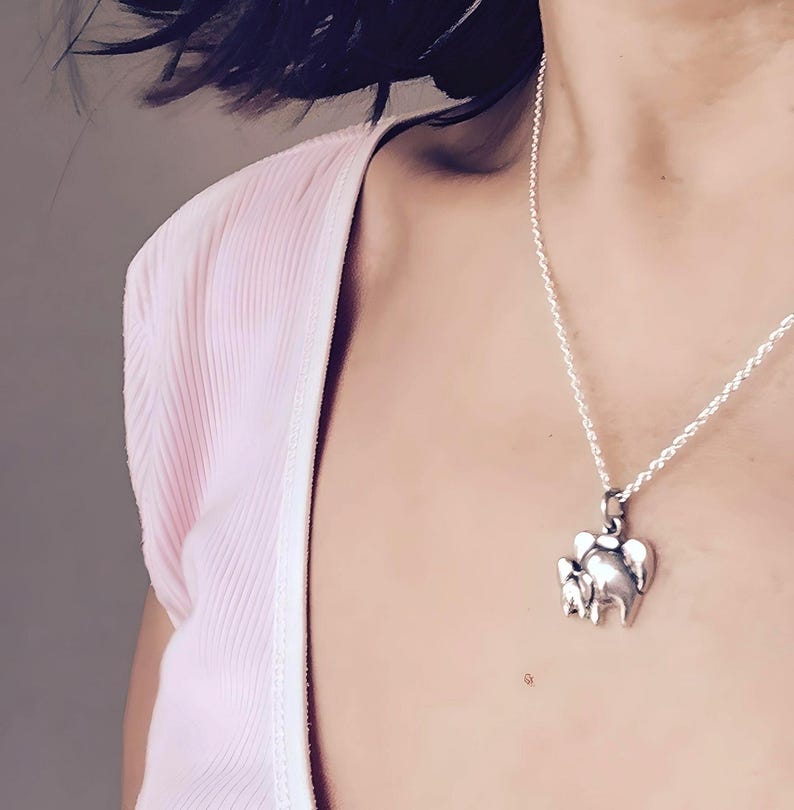 May include: A silver-toned metal pendant shaped like a small elephant, suspended from a delicate silver-toned rope chain necklace. The elephant charm features a smooth, polished surface with subtle indentations defining the ears and trunk.