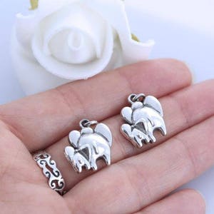 May include: Two silver-toned metal charms, each shaped like a stylized elephant with a smaller elephant beside it, featuring a small jump ring at the top for attachment. A silver-toned ring with an intricate, repeating cutout pattern is also visible.