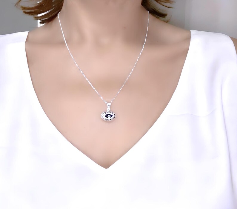 May include: A silver chain necklace with a small, silver eye pendant. The eye is black with a white pupil and is surrounded by a silver frame.