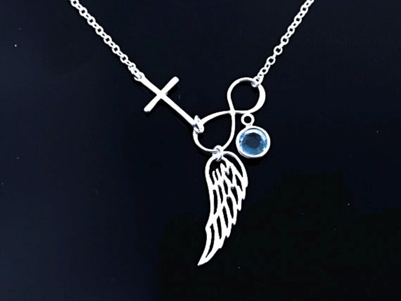 May include: Silver necklace featuring a cross, infinity symbol, and a single blue gemstone. The pendant incorporates a delicate wing design.