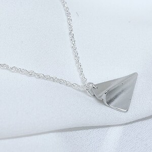 May include: A silver chain necklace with a silver paper airplane pendant.