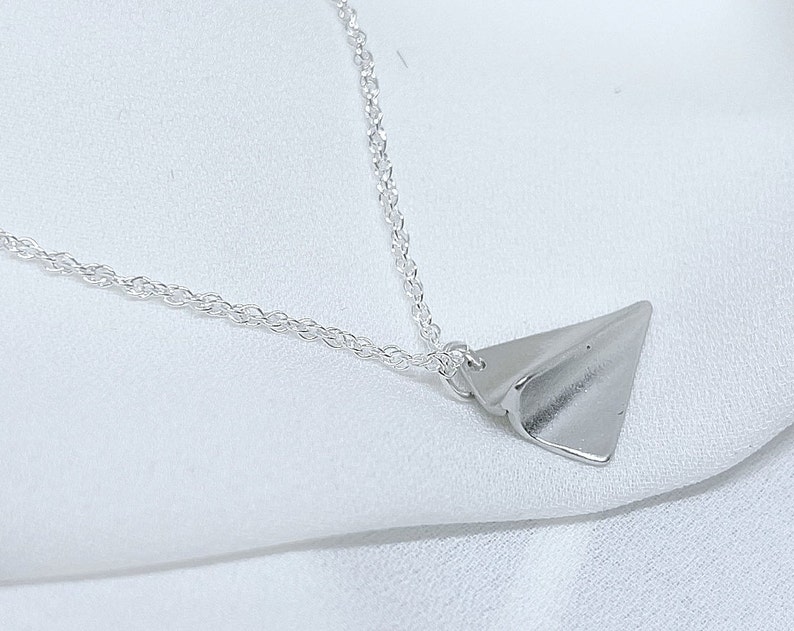 May include: A silver chain necklace with a silver paper airplane pendant.