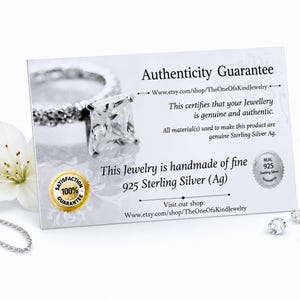 May include: A rectangular white authenticity guarantee card featuring a silver ring with a square-cut stone, a gold 100% satisfaction guarantee seal, and a silver 925 sterling silver seal. The text reads Authenticity Guarantee and 925 Sterling Silver.