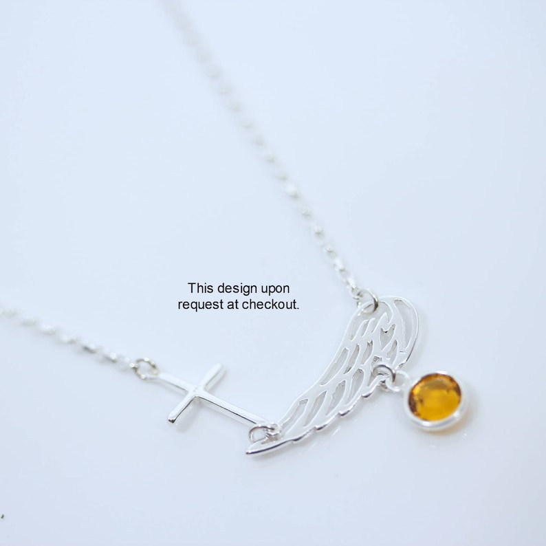 May include: Silver necklace featuring a cross pendant and a wing charm with an amber gemstone. This design is available upon request at checkout.