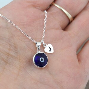May include: A silver chain necklace with a blue evil eye charm and a silver heart charm with the letter "J" on it.