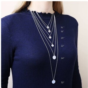 May include: A set of six silver necklaces with circular pendants, each necklace is a different length, ranging from 16 inches to 32 inches. The necklaces are displayed on a model wearing a dark blue sweater.
