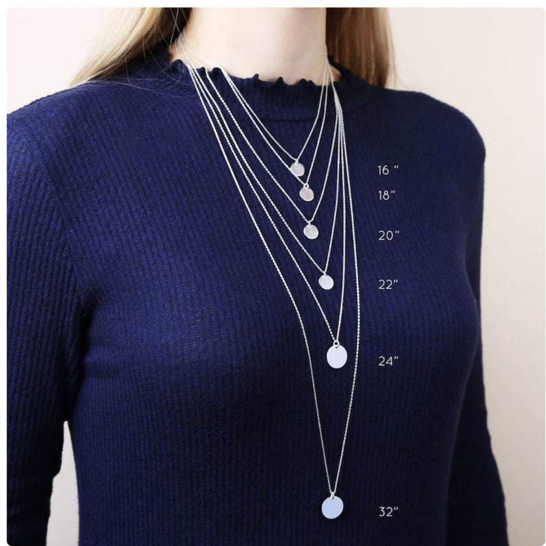 May include: A set of six silver necklaces with circular pendants, each necklace is a different length, ranging from 16 inches to 32 inches. The necklaces are displayed on a model wearing a dark blue sweater.