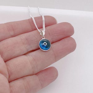 May include: A silver chain necklace with a blue evil eye pendant. The pendant is round and has a white center with a black pupil.