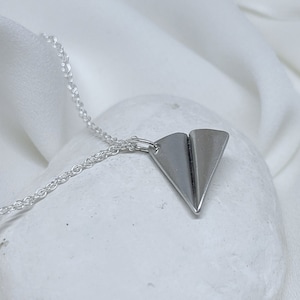 May include: A silver chain necklace with a silver paper airplane pendant.