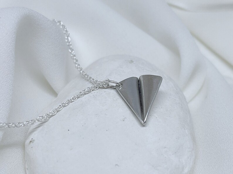 May include: A silver chain necklace with a silver paper airplane pendant.