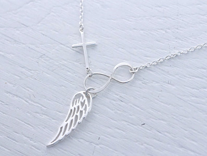 May include: Silver necklace featuring a cross, infinity symbol, and a single wing charm.