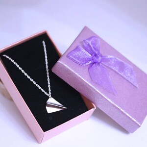 May include: A silver paper airplane necklace in a pink gift box with a purple ribbon.