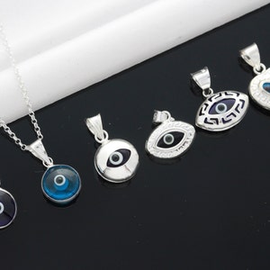 May include: A set of six silver pendants featuring the evil eye symbol. The pendants are in various shapes, including round, oval, and heart. The evil eyes are blue and black, and the pendants are on silver chains.