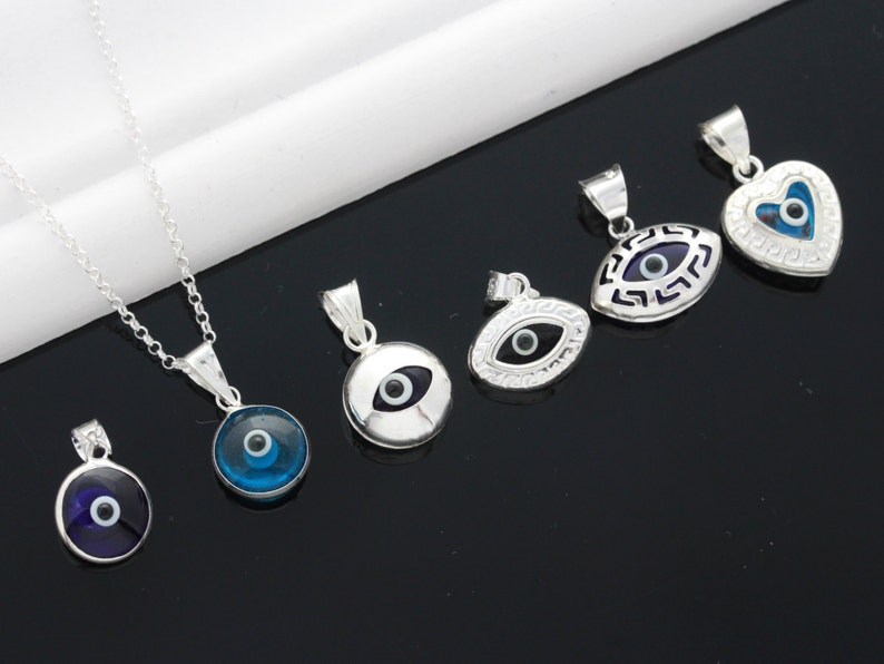May include: A set of six silver pendants featuring the evil eye symbol. The pendants are in various shapes, including round, oval, and heart. The evil eyes are blue and black, and the pendants are on silver chains.