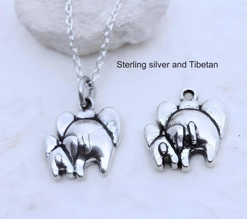May include: A silver-toned necklace featuring a pendant shaped like two elephants, accompanied by a separate matching elephant charm. The text "Sterling silver and Tibetan" is visible. The pendant hangs from a delicate silver-toned chain.
