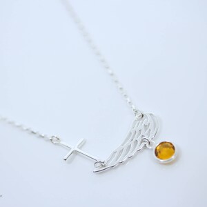 May include: A silver necklace with a cross pendant, a wing pendant, and a small amber-coloured gemstone.