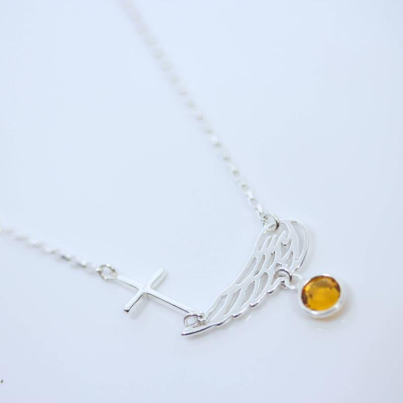 May include: A silver necklace with a cross pendant, a wing pendant, and a small amber-coloured gemstone.