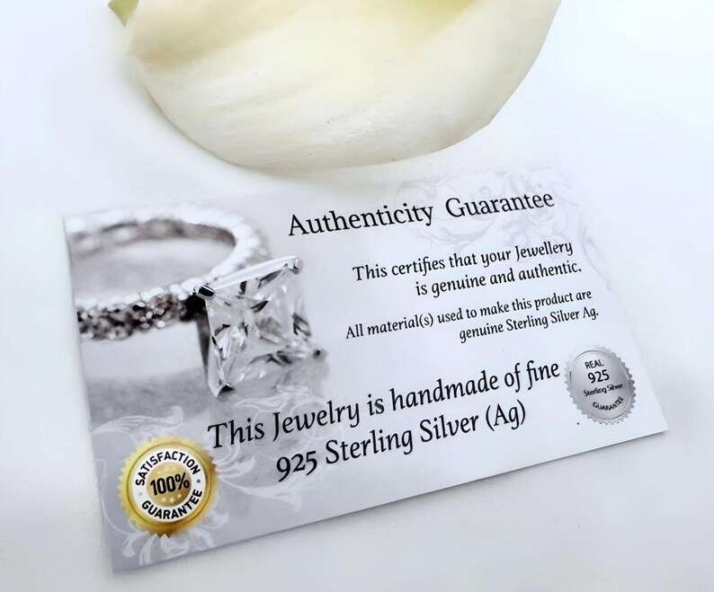 May include: A white card with the text "Authenticity Guarantee" and "This certifies that your Jewellery is genuine and authentic. All material(s) used to make this product are genuine Sterling Silver Ag. This Jewelry is handmade of fine 925 Sterling Silver (Ag)". A silver ring with a square-shaped stone is pictured on the card. The card also has a 100% Satisfaction Guarantee seal and a Real 925 Sterling Silver Guarantee seal.