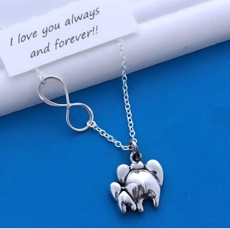 May include: A silver-toned necklace featuring an infinity symbol charm and a small elephant-shaped pendant. A white rectangular card is attached to the chain, displaying the printed black text: I love you always and forever!!