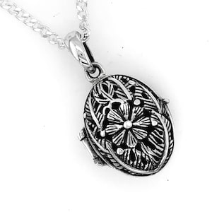 May include: Silver oval locket pendant with a floral design, suspended from a fine chain. The pendant showcases an intricate openwork pattern, featuring a central flower and leaf details. The locket is made of silver.