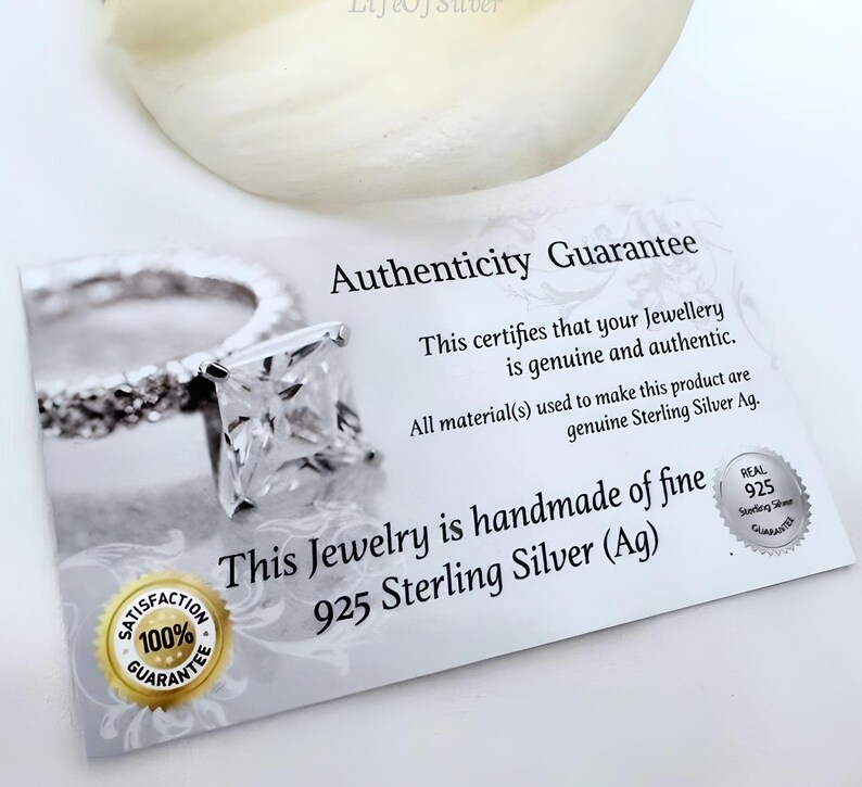 Puede incluir: Una tarjeta blanca con el texto "Authenticity Guarantee" y "This certifies that your Jewellery is genuine and authentic. All material(s) used to make this product are genuine Sterling Silver Ag. This Jewelry is handmade of fine 925 Sterling Silver (Ag)" impreso en ella. La tarjeta tambi&eacute;n tiene un peque&ntilde;o c&iacute;rculo plateado con el texto "REAL 925 Sterling Silver GUARANTEE" impreso en &eacute;l.