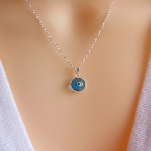 May include: A silver chain necklace with a blue evil eye pendant. The pendant is round and has a white center.