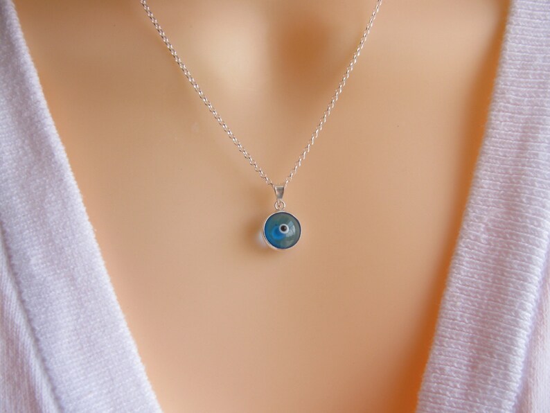 May include: A silver chain necklace with a blue evil eye pendant. The pendant is round and has a white center.
