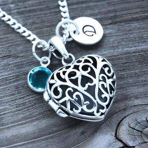 Puede incluir: Un collar de plata con un dije en forma de coraz&oacute;n, una peque&ntilde;a gema turquesa y un dije con la letra "D".