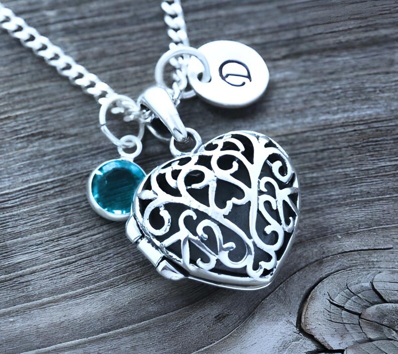 Puede incluir: Un collar de plata con un dije en forma de coraz&oacute;n, una peque&ntilde;a gema turquesa y un dije con la letra "D".