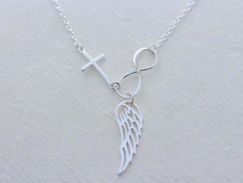 May include: Silver necklace featuring a cross, infinity symbol, and a single wing pendant.