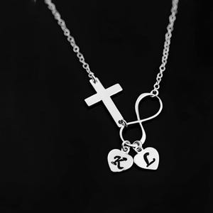 May include: Silver necklace with a cross, infinity symbol, and two heart charms with the letters K and L.