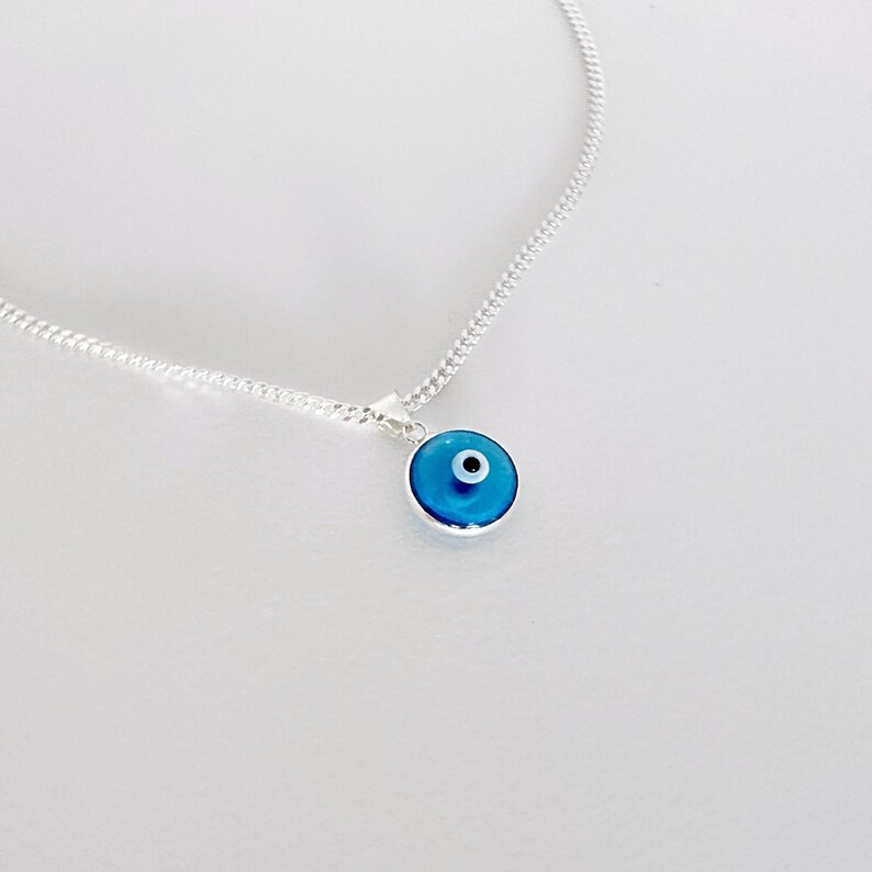 May include: A silver chain necklace with a blue evil eye pendant. The pendant is round and has a white center.
