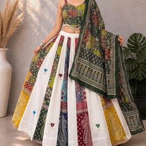May include: A two-piece ensemble featuring a sleeveless crop top and a floor-length skirt, both decorated with a multi-colored patchwork pattern of paisley and floral motifs. The skirt includes white panels and small triangular mirror accents.