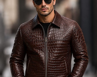 May include: A dark brown leather jacket featuring a textured crocodile skin pattern, a classic collar, and a full-length front zipper. The jacket is worn over a black shirt and paired with dark trousers, complemented by dark-tinted aviator sunglasses.