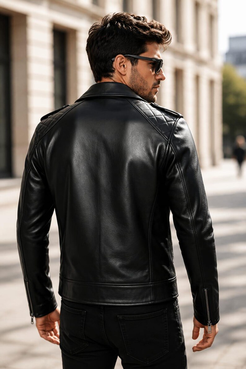 May include: A black leather jacket featuring a quilted pattern on the shoulders, a fold-down collar, and silver-toned metal zippers on the sleeve cuffs. The jacket is worn over black pants, showcasing a smooth finish and structured design.