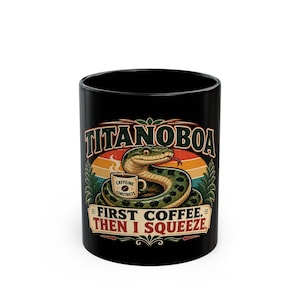 Peut inclure: Un mug en céramique noire orné d'un dessin de serpent vert enroulé autour d'une tasse de café. Le texte TITANOBOA figure en haut et FIRST COFFEE. THEN I SQUEEZE. en bas. La tasse de café porte l'inscription CAFFEINE CONSTRICTS.
