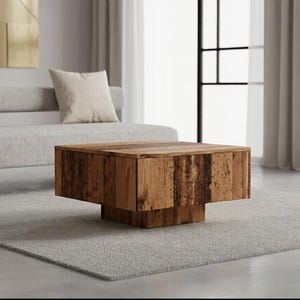Peut inclure: Une table basse carrée fabriquée en bois naturel avec un grain visible et une finition texturée. La table présente un plateau épais en forme de bloc soutenu par une base carrée plus petite et encastrée, créant un aspect flottant.