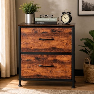 May include: A two-drawer filing cabinet with a rustic brown wood grain finish and a black metal frame. Each drawer features a curved black handle. The top surface holds a potted plant, black eyeglasses, and two books titled Nordic Interiors Homes and Kinfolk.