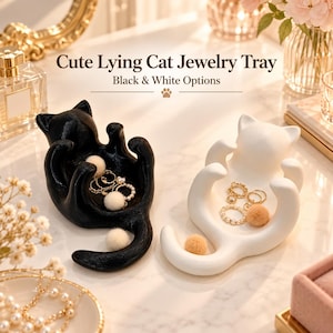 Könnte beinhalten: Zwei Schmuckschalen in Form von liegenden Katzen, eine in Schwarz und eine in Weiß, jeweils mit einem geschwungenen Körper zur Aufbewahrung kleiner Gegenstände. Der Text Cute Lying Cat Jewelry Tray Black & White Options steht darüber.
