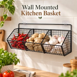 Op de afbeelding: Een zwarte metalen wand-keukenmand met drie draadcompartimenten. De tekst Wall Mounted Kitchen Basket staat erboven. De mand bevat rode pepers, gemberwortels en knoflookbollen en is bevestigd aan een witte betegelde muur.